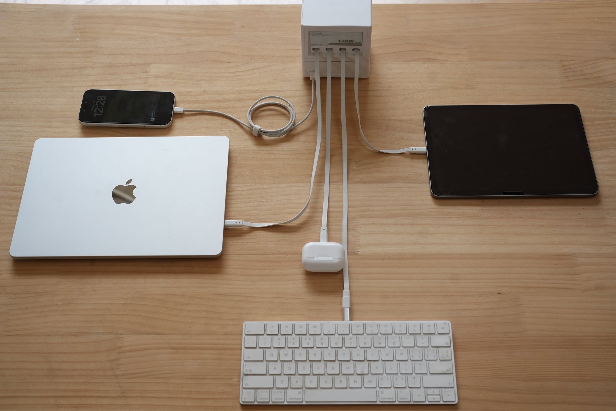 Gitryin Nexus charging station on a wooden desk, charging a laptop, phone, tablet, earbuds and keyboard through its retractable cables
